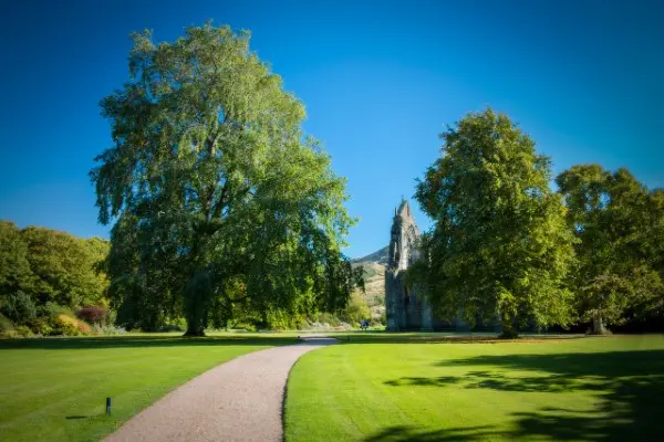 Lush greenery and vibrant flower beds in the gardens of the Palace of Holyroodhouse, with Arthur's Seat in the background.